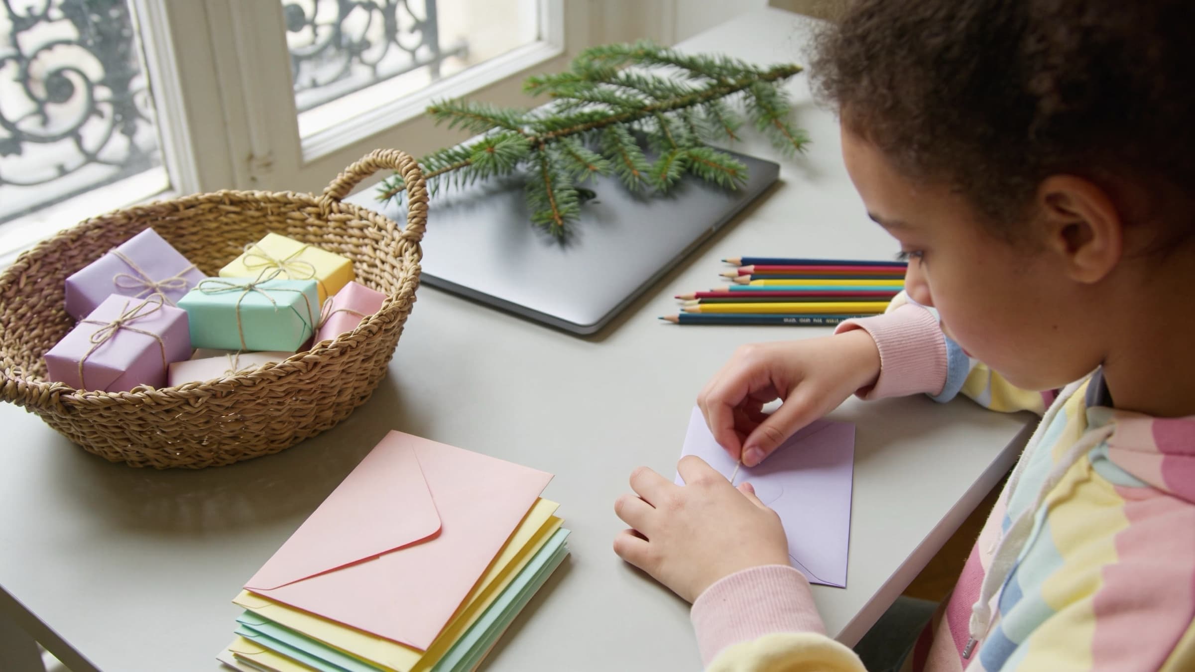 Bureau en décembre : panier de petits cadeaux emballés de papier pastel, enveloppes scellées et branche de sapin